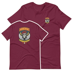 May include: Maroon t-shirts with a graphic design. The front of the shirt has a small patch with a skull and wings. The back of the shirt has a larger design with the word "AIRBORNE" and the phrase "DEATH FROM ABOVE".