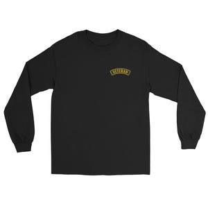 May include: Black long-sleeve shirt with the word "VETERAN" in gold lettering on the upper left chest. The shirt has a crew neck and long sleeves.