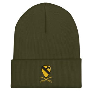 Könnte beinhalten: Olivgrüne Beanie-Mütze mit umgeschlagenem Saum. Auf der Vorderseite befindet sich ein gesticktes Emblem mit einem schwarz-gelben Schild, einem Pferd und gekreuzten Säbeln. Eine warme, lässige Mütze.