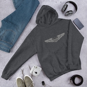 May include: A dark gray hooded sweatshirt with a white embroidered design of a pair of wings with a shield in the center. The shield has a design that resembles the American flag.