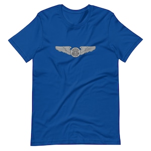 May include: Royal blue t-shirt featuring a silver-colored pilot's wings emblem. The emblem is centered on the chest and includes a circular design with the US seal. The wings are spread out on either side of the seal.