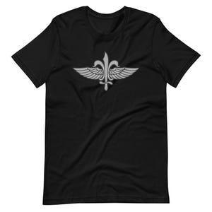 May include: A black short-sleeve t-shirt featuring a centered graphic of a silver fleur-de-lis emblem with stylized wings extending from the sides. The design is printed in a light grey tone, contrasting against the solid black fabric of the shirt.
