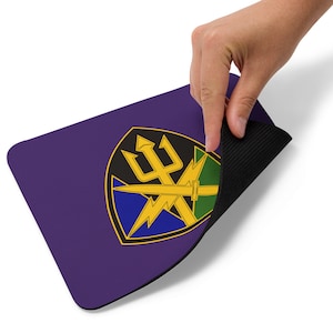 May include: A purple mouse pad with a black rubber backing. The mouse pad features a yellow, green, blue, and black military insignia with a trident and lightning bolts.