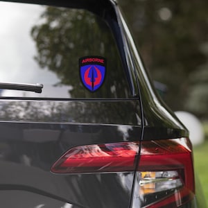 May include: A black car with a red and blue "AIRBORNE" sticker on the back window. The sticker features a stylized sword and wings.