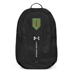 May include: Black Under Armour backpack with a green and red patch featuring the number "1". The backpack has a top handle, side mesh pockets, and the Under Armour logo in silver. The word "STORM" is printed at the bottom.