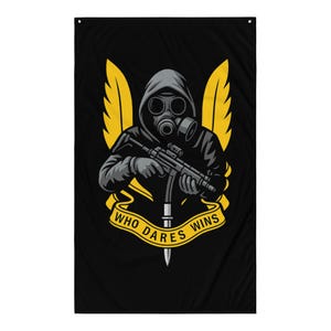 Op de afbeelding: Zwarte vlag met een afbeelding van een figuur met een gasmasker en capuchon die een geweer vasthoudt, geflankeerd door gele vleugels. De tekst "WHO DARES WINS" staat op een gele banner eronder.