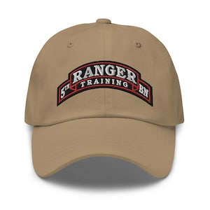 Könnte beinhalten: Eine beige Baseballkappe mit einem gestickten Aufnäher, auf dem "5th Ranger Training Bn" in weißer und roter Schrift steht.