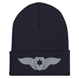 May include: A navy blue beanie with a gray embroidered patch featuring a star of David inside a shield with wings on either side.