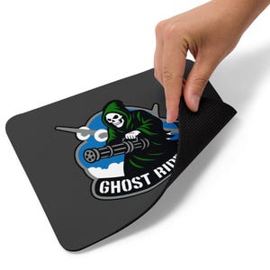 May include: A black rectangular mousepad with a graphic of a grim reaper in a green hooded cloak, holding a machine gun. The design includes the text "GHOST RIDER" in white, with a blue and white background.