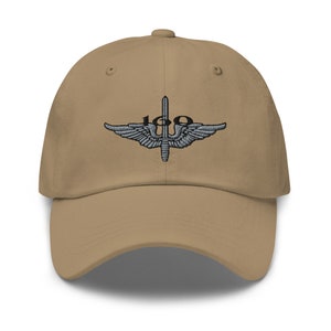 May include: A tan baseball cap with an embroidered patch featuring a silver sword and wings with the number "100" in black.