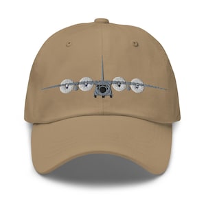 May include: A tan baseball cap with an embroidered image of a military cargo plane. The plane is gray and has four propellers.