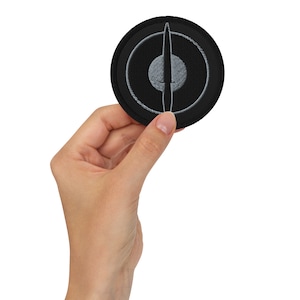 May include: Black embroidered patch with a silver circle and a silver knife in the center.