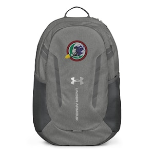 Peut inclure: Sac à dos gris Under Armour avec un écusson circulaire représentant une figure avec une flamme et des détails bleus et blancs. Le sac à dos a des poches latérales en filet, une poignée supérieure et le logo Under Armour.