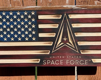May include: Wooden American flag with the United States Space Force logo. The flag features a blue field with white stars, red and white stripes, and the Space Force emblem. The words "UNITED STATES SPACE FORCE" are below the emblem.