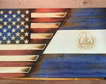 May include: A wooden sign with the American flag on the left side and the flag of El Salvador on the right side. The flags are burned into the wood and have a distressed look. The El Salvador flag has the country's coat of arms in the center.