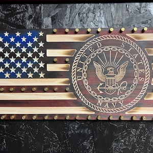 May include: A wooden American flag with a distressed finish, featuring the United States Navy seal in the center. The flag is decorated with brass bullet casings.