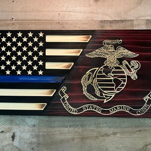 May include: A wooden American flag with a blue line and the United States Marine Corps emblem. The flag is stained in a dark wood color and the emblem is in gold.