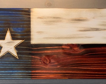 May include: A wooden Texas flag with a white star in the blue section, a white middle section, and a red bottom section. The wood has a distressed look with visible grain.