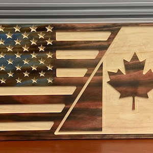 May include: A wooden sign with the American and Canadian flags carved into it. The American flag is on the left side of the sign and the Canadian flag is on the right side. The flags are both carved in a dark wood with light wood accents.