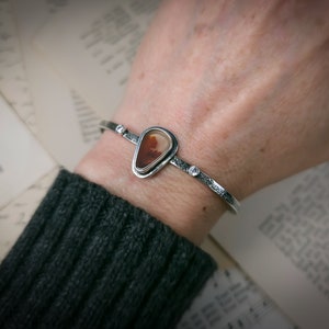Puede incluir: Un brazalete de plata con una piedra de &aacute;gata en forma de l&aacute;grima engastada en un bisel de plata. El brazalete tiene tres peque&ntilde;os detalles de plata.
