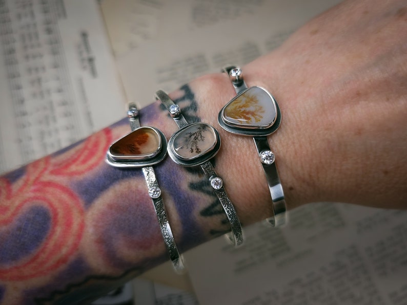 Puede incluir: Tres pulseras de plata con detalles de piedra de &aacute;gata. Cada pulsera presenta una piedra de &aacute;gata diferente con patrones y colores &uacute;nicos. Las pulseras est&aacute;n adornadas con peque&ntilde;as piedras preciosas transparentes.
