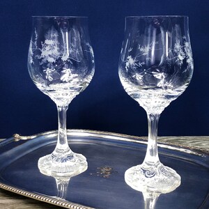 May include: Two clear wine glasses with etched floral designs sit on a silver oval tray. The tray has a beaded edge and rests on three small feet. The background is a dark blue.