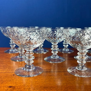 May include: A collection of clear, stemmed champagne glasses with a textured, cut-glass design. The glasses have a round bowl and a decorative stem, set against a blue background.
