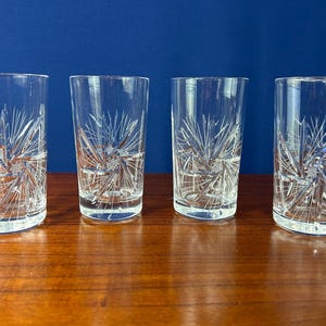 May include: A white ceramic mug with a black handle and the text "But First, Coffee" in a bold, black font. The mug is filled with a dark liquid, likely coffee, and sits on a light-colored surface.