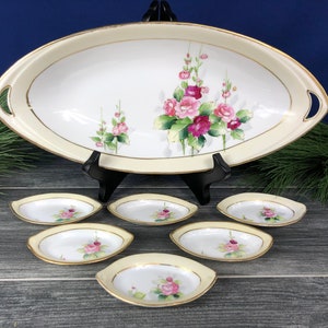 May include: A vintage serving platter and matching small dishes. The oval platter and dishes have a cream-colored border with gold trim. Each piece is decorated with pink and magenta roses and green leaves.