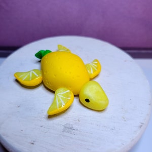 May include: A yellow lemon-shaped turtle figurine with green leaves on top and white details on the shell. The figurine is on a white surface.