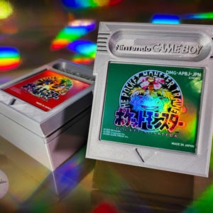 May include: A white Game Boy cartridge case and a matching game cartridge. The cartridge features a green label with Japanese text and the words "POCKET MONSTER TRAINER". The Game Boy case has the Nintendo Game Boy logo.