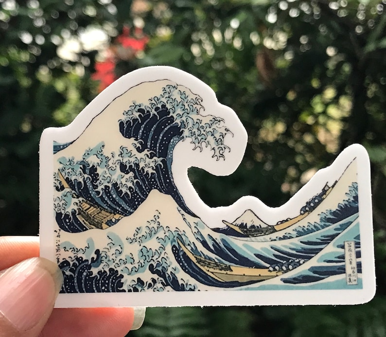 Pu&ograve; includere: Un adesivo con un'illustrazione dettagliata di un'onda gigante, ispirata alla famosa stampa giapponese su legno "La Grande Onda di Kanagawa" di Katsushika Hokusai. L'onda &egrave; rappresentata in tonalit&agrave; di blu e bianco, con una barca tradizionale giapponese e il monte Fuji sullo sfondo.