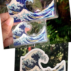 Pu&ograve; includere: Tre adesivi con la Grande Onda di Kanagawa in diverse dimensioni. Gli adesivi sono stampati su carta bianca con uno strato protettivo trasparente. Gli adesivi mostrano un'onda blu e bianca con il Monte Fuji sullo sfondo.
