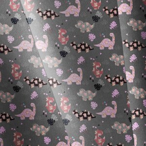 May include: A dark gray fabric featuring a repeating pattern of light pink and black dinosaurs interspersed with small tropical leaves and geometric triangles. The dinosaurs are depicted in various poses, including long-necked and spiked varieties.