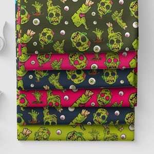 May include: A stack of six folded fabric swatches featuring a repeating pattern of green zombie heads, severed hands, and eyeballs. The background colors of the fabric layers alternate between dark olive, bright pink, and dark navy blue.