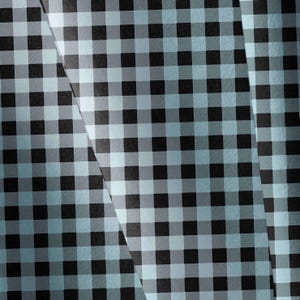 May include: A fabric featuring a classic gingham pattern composed of alternating black and light blue squares. The material is displayed in overlapping layers, creating a visual effect of folded sections with varying light and shadow across the surface.