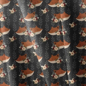 May include: A dark gray fabric featuring a repeating pattern of orange fox heads with closed eyes, each adorned with small white and red flowers, interspersed with vertical columns of light gray stylized leaf sprigs in a continuous design.