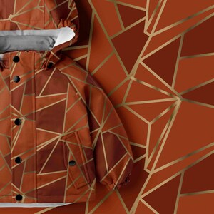 Puede incluir: Una chaqueta con capucha que presenta un patrón geométrico de líneas doradas que se cruzan sobre un fondo de color óxido. La chaqueta incluye una tapeta frontal con cinco botones circulares negros, mangas largas y un forro interior blanco.