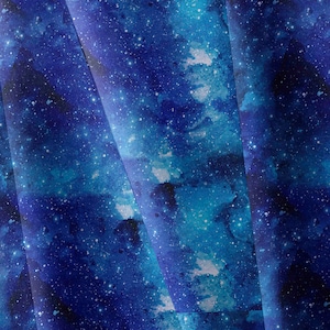 May include: A fabric or paper sheet featuring a deep blue and indigo galaxy print. The design displays a watercolor-style nebula effect with scattered white specks representing stars, creating a layered cosmic appearance across the surface.