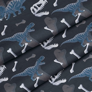 May include: Dark grey fabric featuring a repeating pattern of blue dinosaurs, white dinosaur skulls, and white bones. The dinosaurs include a T-Rex, Triceratops, and other species. The fabric has a slight sheen.