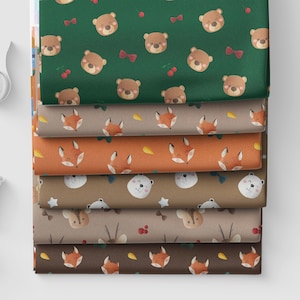 Puede incluir: Una pila de seis rollos de tela plegados con patrones repetitivos de animales del bosque. Los diseños incluyen osos pardos con lazos rojos y cerezas sobre verde, zorros con zanahorias sobre naranja y osos blancos con estrellas sobre marrón.
