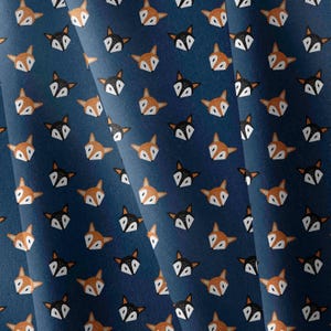 May include: A dark blue fabric featuring a repeating pattern of stylized fox heads. The foxes alternate between orange with white accents and black with white accents, all oriented in the same direction across the textile surface.