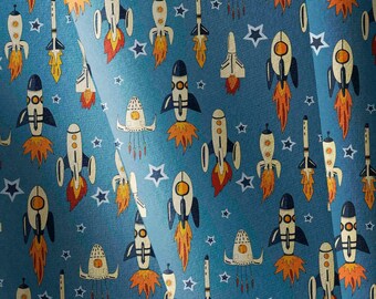 May include: A blue fabric featuring a repeating pattern of various white and black rockets with orange flames, interspersed with white star shapes. The rockets are depicted in different orientations and styles, creating a dense space-themed design.