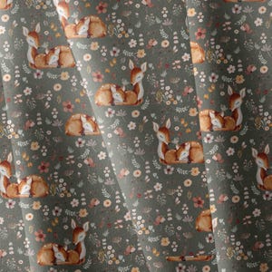 May include: A fabric featuring a repeating pattern of sleeping brown fawns interspersed with small white, pink, and orange flowers, along with green foliage on a dark sage green background. The design includes multiple deer in various positions.
