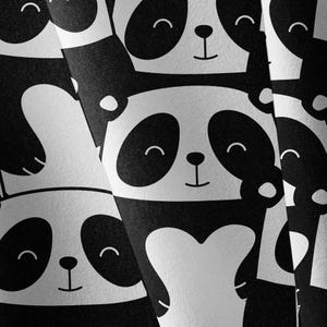 May include: A repeating pattern of stylized panda faces in black and white. Each panda features large black eye patches, a small black nose, and a simple curved line for a mouth. The design is printed on a textured fabric surface.