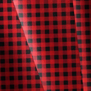 May include: A fabric surface featuring a classic red and black buffalo check plaid pattern. The design consists of alternating square blocks of solid red and solid black, creating a repeating grid layout across the entire visible material texture.
