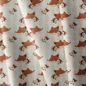 May include: A fabric featuring a repeating pattern of orange fox heads with closed eyes, each adorned with a cluster of small cream and dark red flowers, set against a light cream background with vertical rows of pale beige leaf silhouettes.