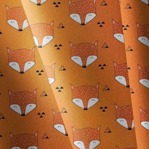 May include: A fabric pattern featuring repeating orange and white fox faces with closed eyes and small black triangular shapes scattered across a textured orange background. The design displays a consistent, symmetrical arrangement of fox heads.