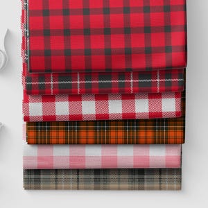 May include: A stack of six folded fabric pieces featuring various plaid and gingham patterns. The designs include red and black buffalo check, red and white gingham, orange and black plaid, pink and white gingham, and tan and black plaid.