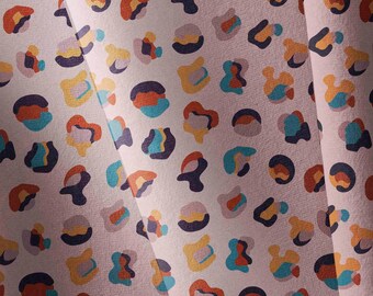 May include: A fabric featuring a repeating abstract leopard print pattern on a light pink background. The spots consist of layered, irregular shapes in shades of dark blue, teal, orange, and yellow, creating a multi-coloured, textured appearance.